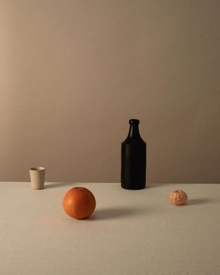 an orange sitting next to a black bottle on a table