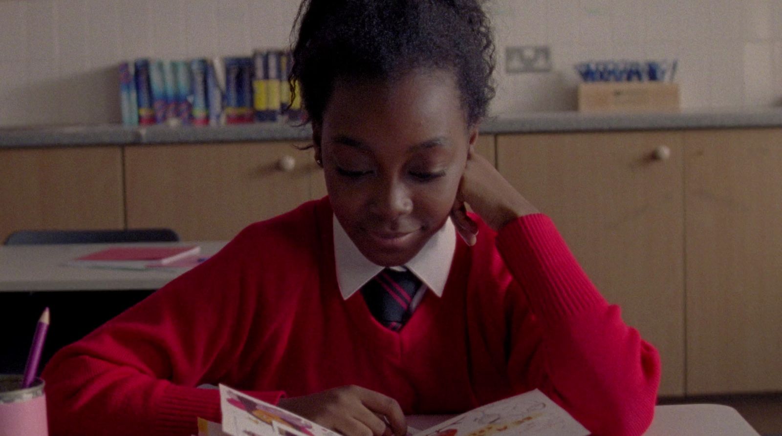 a young girl sitting at a desk reading a book