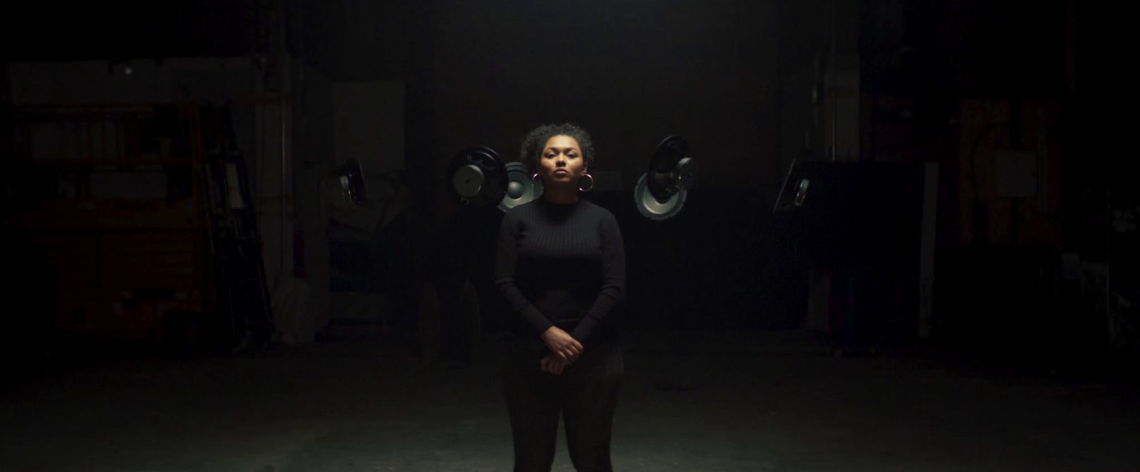 a woman standing in a dark room in front of speakers