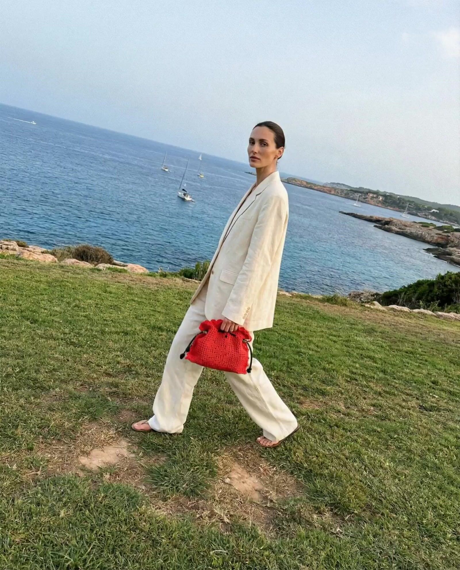 a man in a white suit and red bag walking on grass