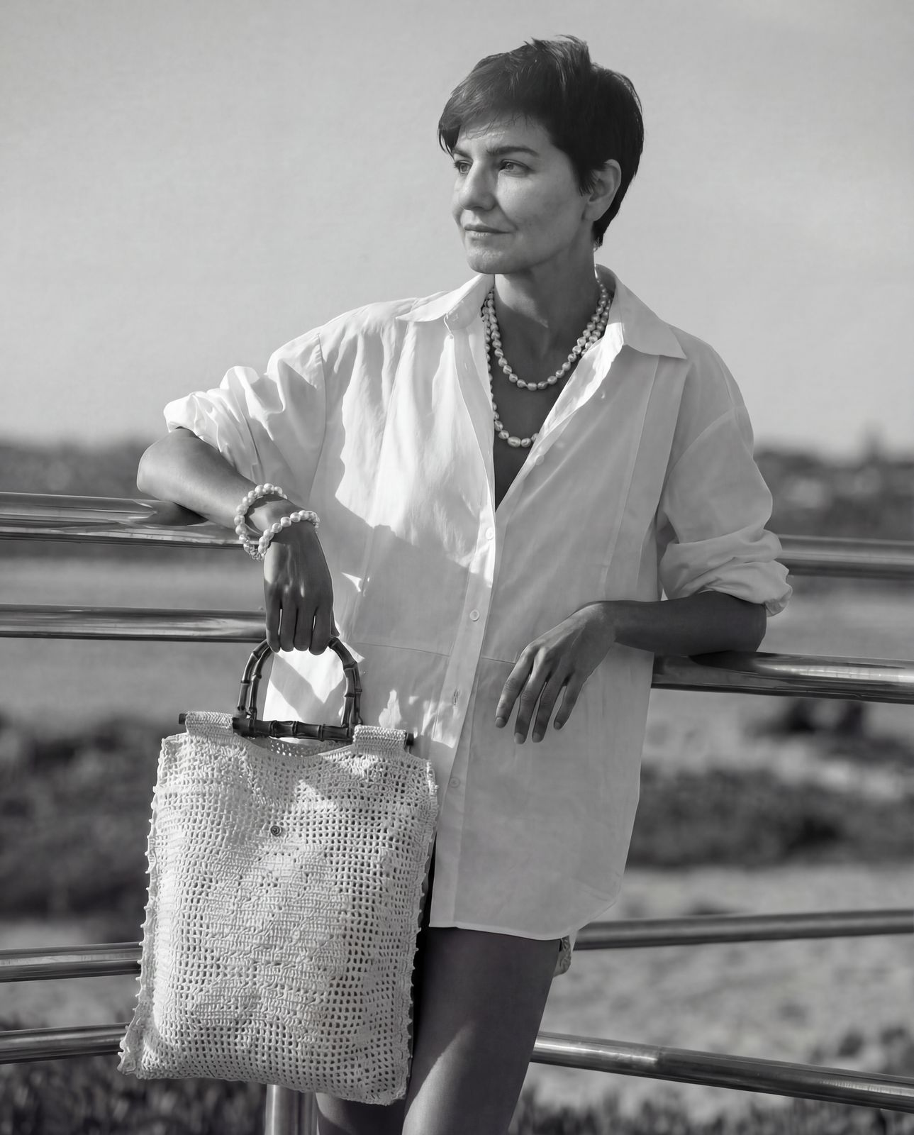 a woman holding a purse standing next to a fence
