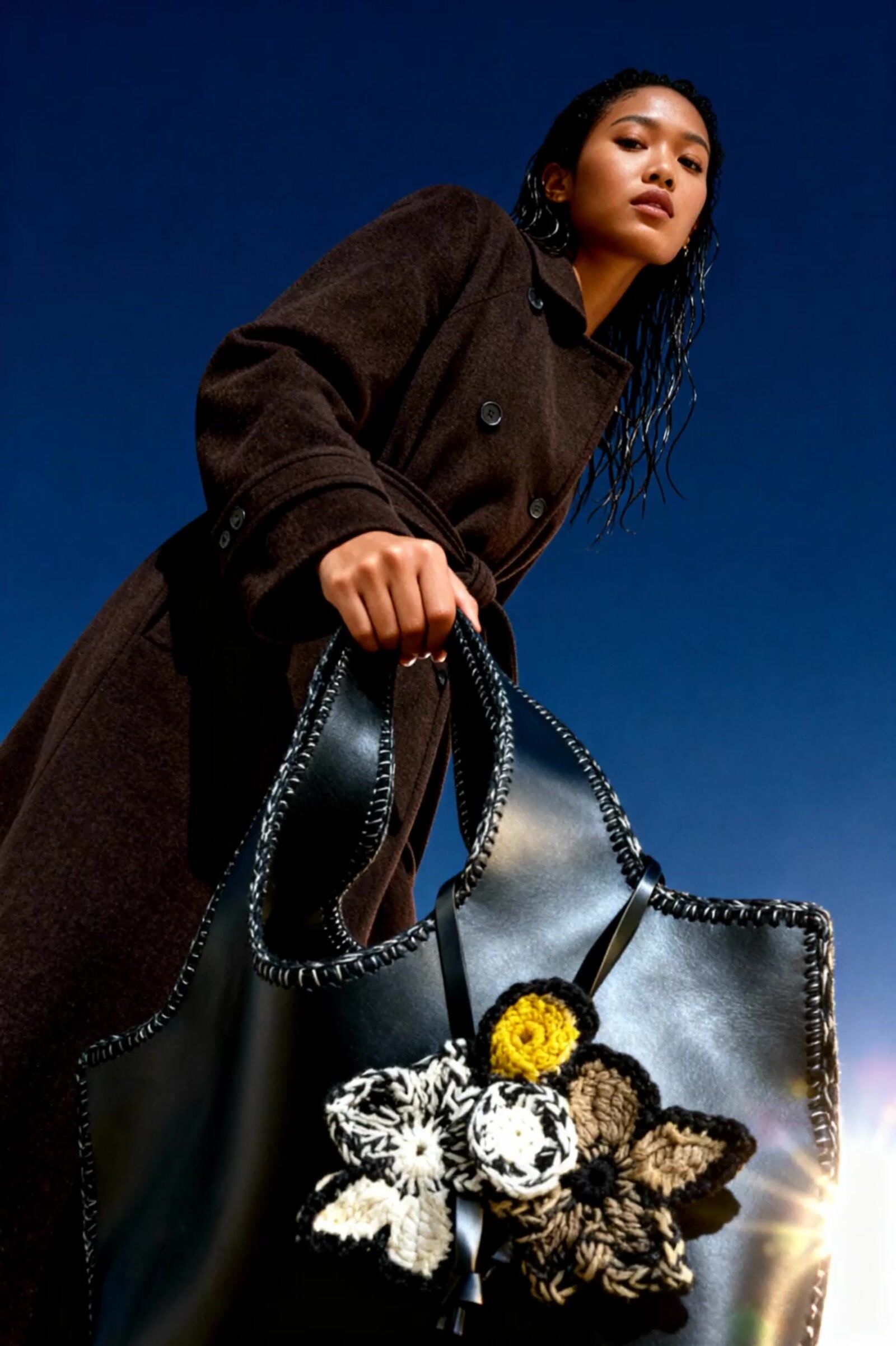 a woman holding a black purse with flowers on it