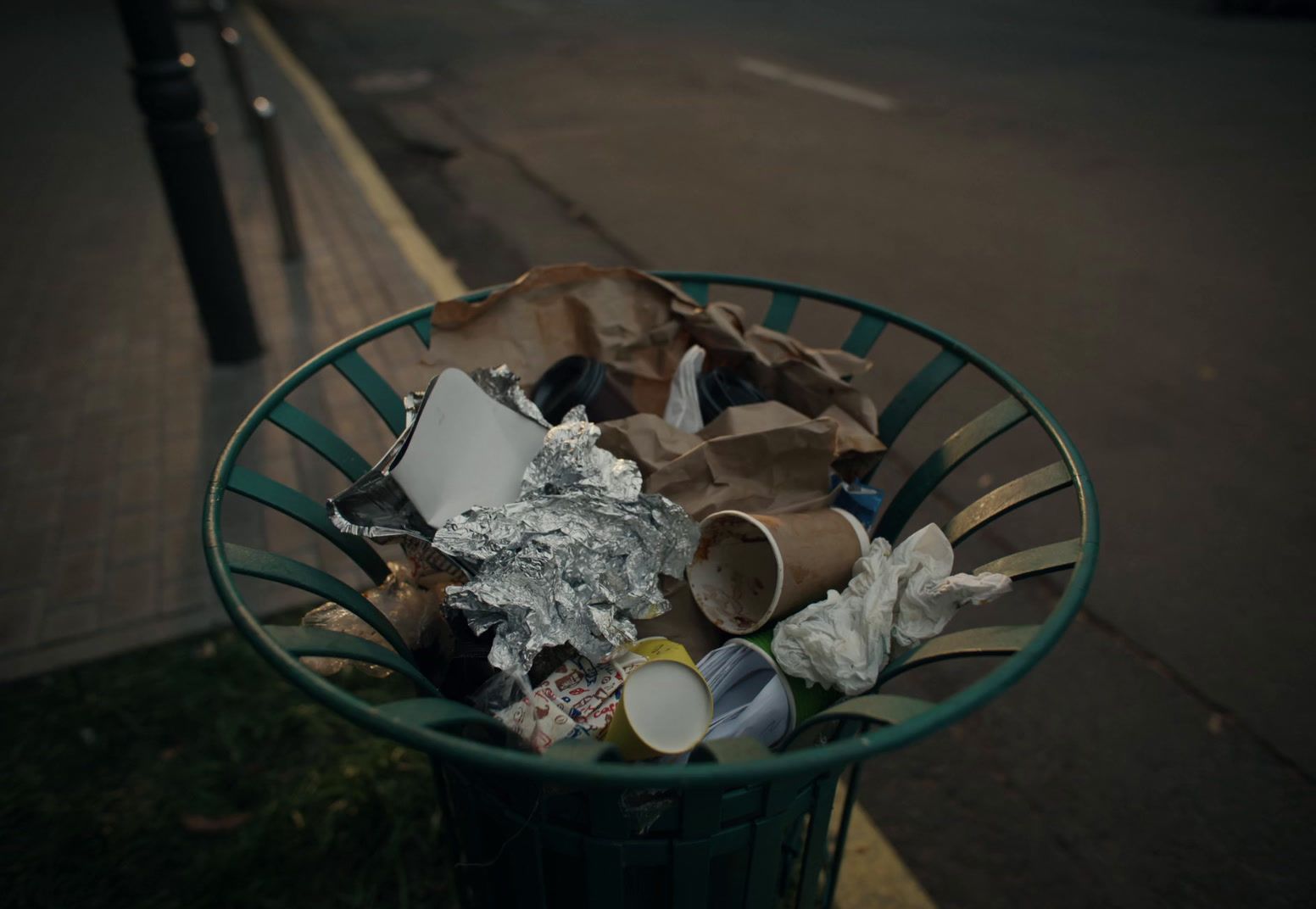 a green trash can filled with garbage on the side of the road