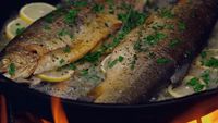 two fish in a skillet with lemon slices and parsley