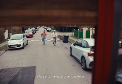 a couple of people walking down a street next to parked cars