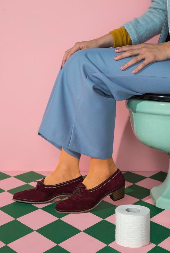 a woman sitting on a toilet next to a roll of toilet paper