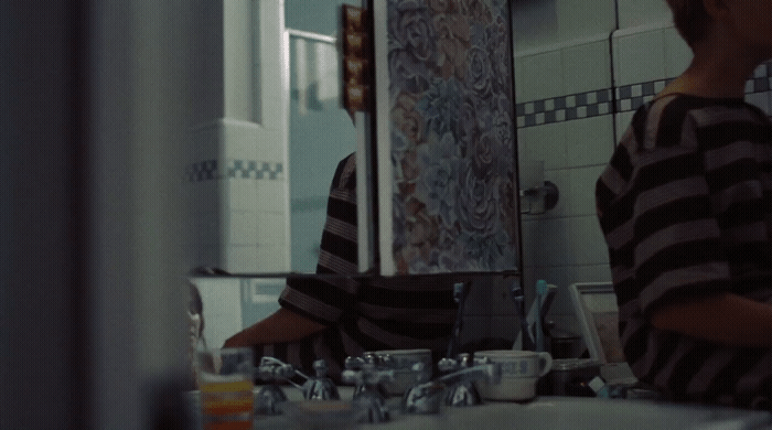 a young boy standing in front of a bathroom mirror