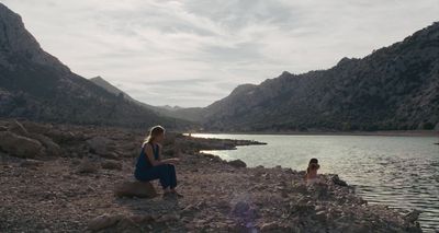 a woman standing on a rocky shore next to a body of water