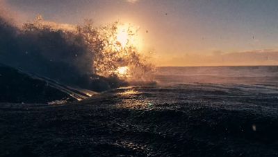 a large wave crashing into the ocean at sunset