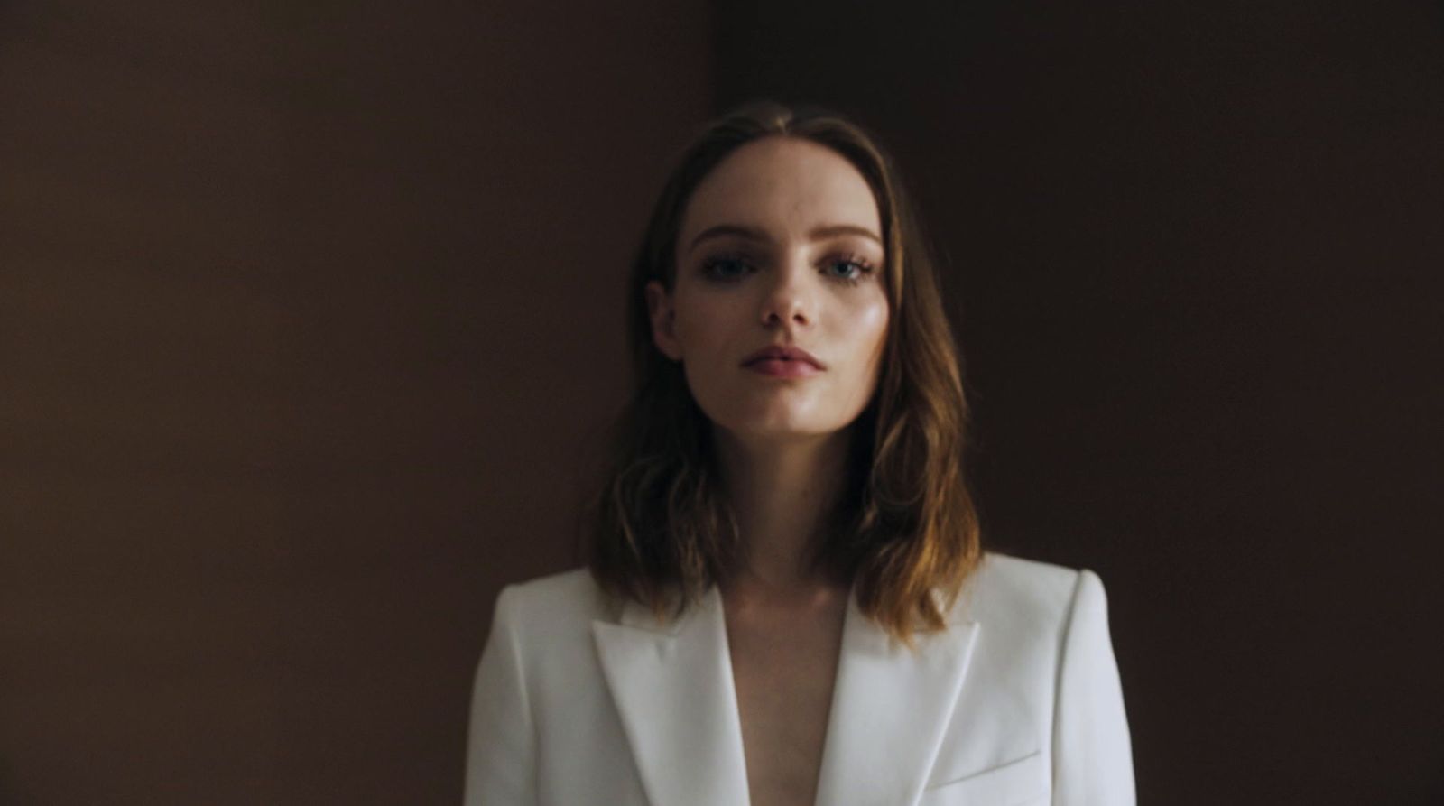 a woman in a white suit standing in front of a wall