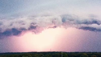 a large cloud looms in the sky over a field