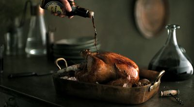 a person pouring a bottle of wine over a roasted turkey