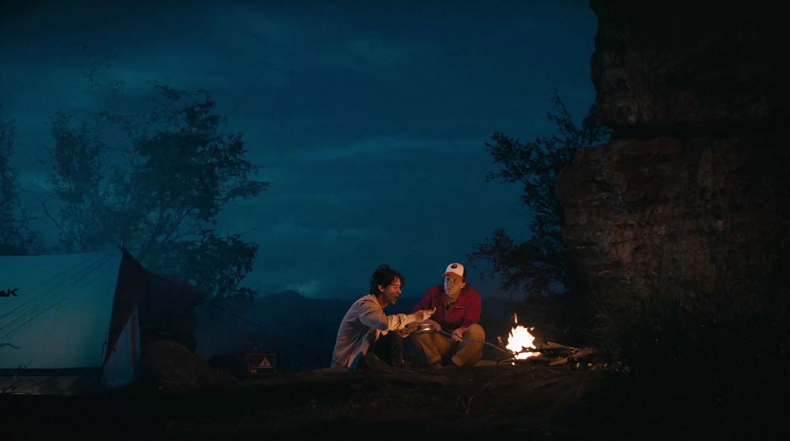 two people sitting around a campfire at night