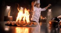 a chef standing in front of a fire in a kitchen