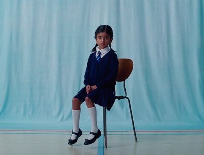 a young girl sitting on a chair in front of a blue backdrop