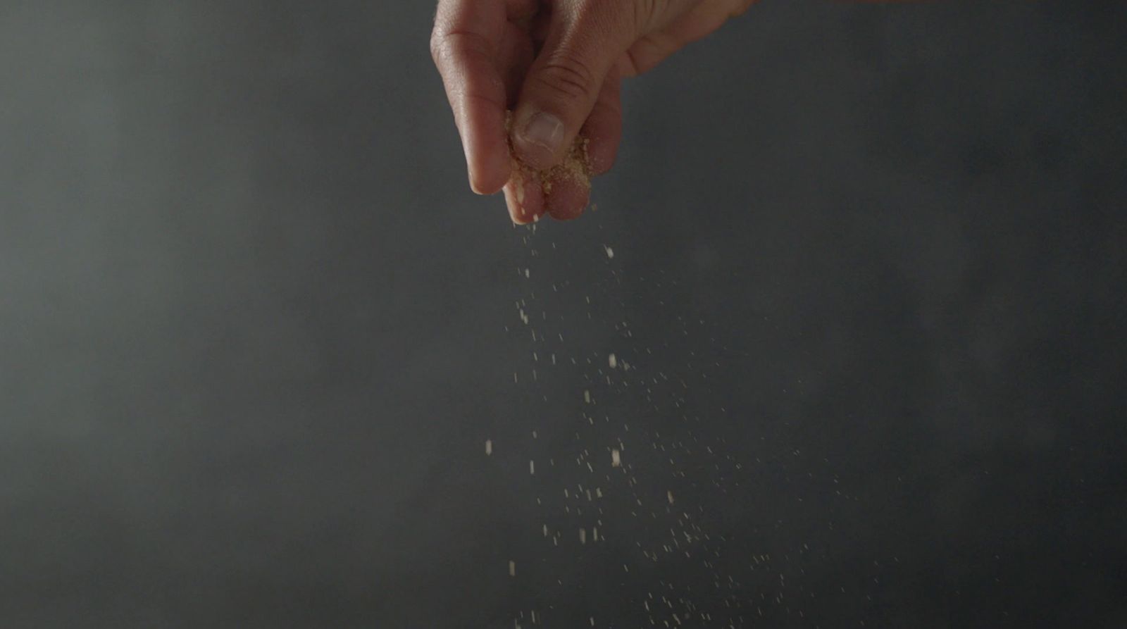 a hand is sprinkled with sand on a dark background