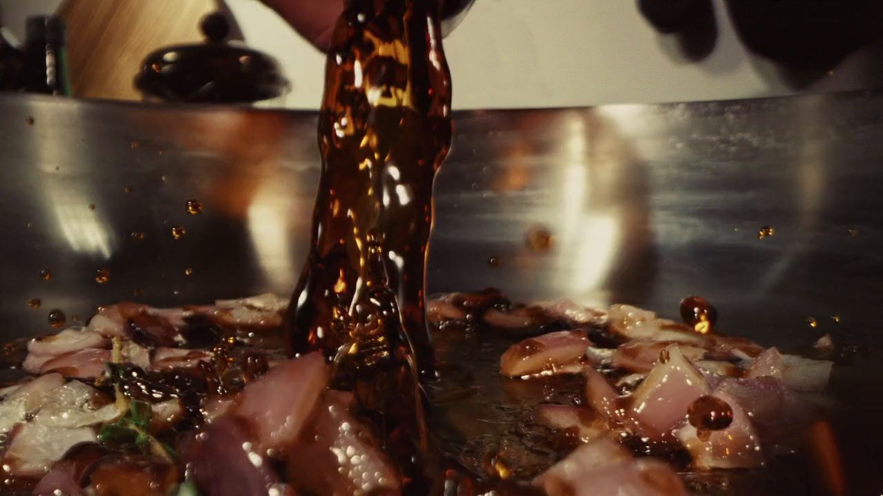 a person pouring sauce on food in a frying pan