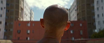 a man with a bald head standing in front of tall buildings