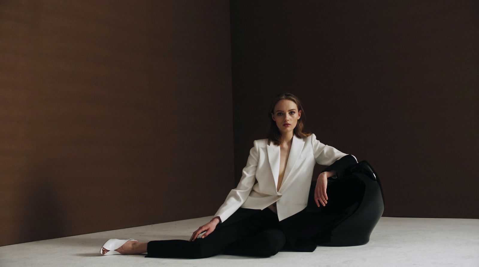 a woman in a white jacket and black pants sitting on the floor