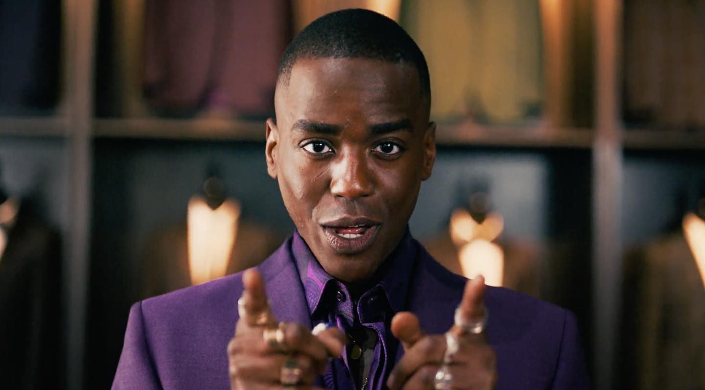 a man in a purple suit pointing to the camera