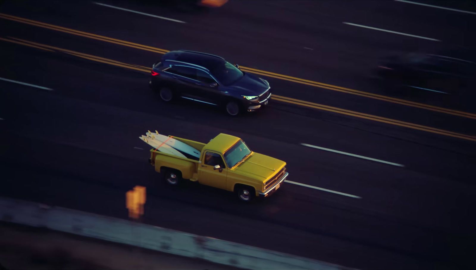 a yellow truck driving down a street next to a black car