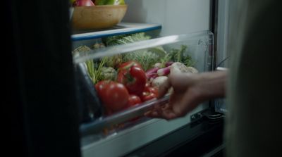 a person reaching into an open refrigerator filled with vegetables