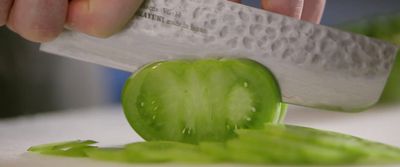 a person cutting a cucumber with a knife