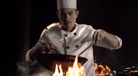 a man in a chef's hat cooking over a fire