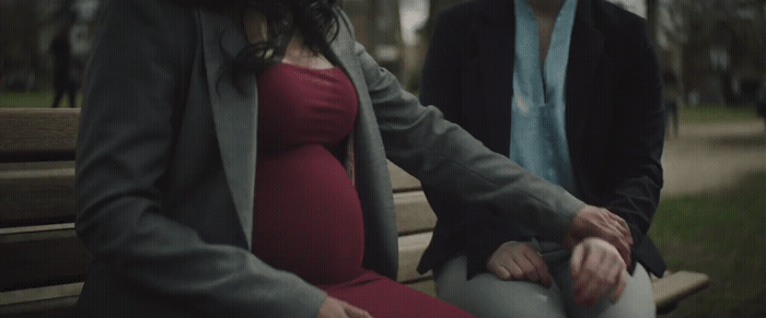 a pregnant woman sitting on a bench next to a man