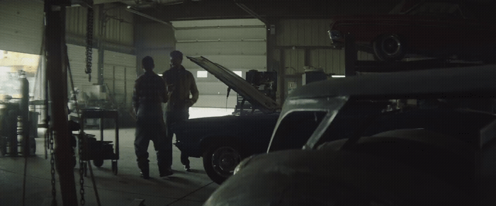 a couple of men standing next to a car in a garage