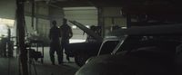 a couple of men standing next to a car in a garage