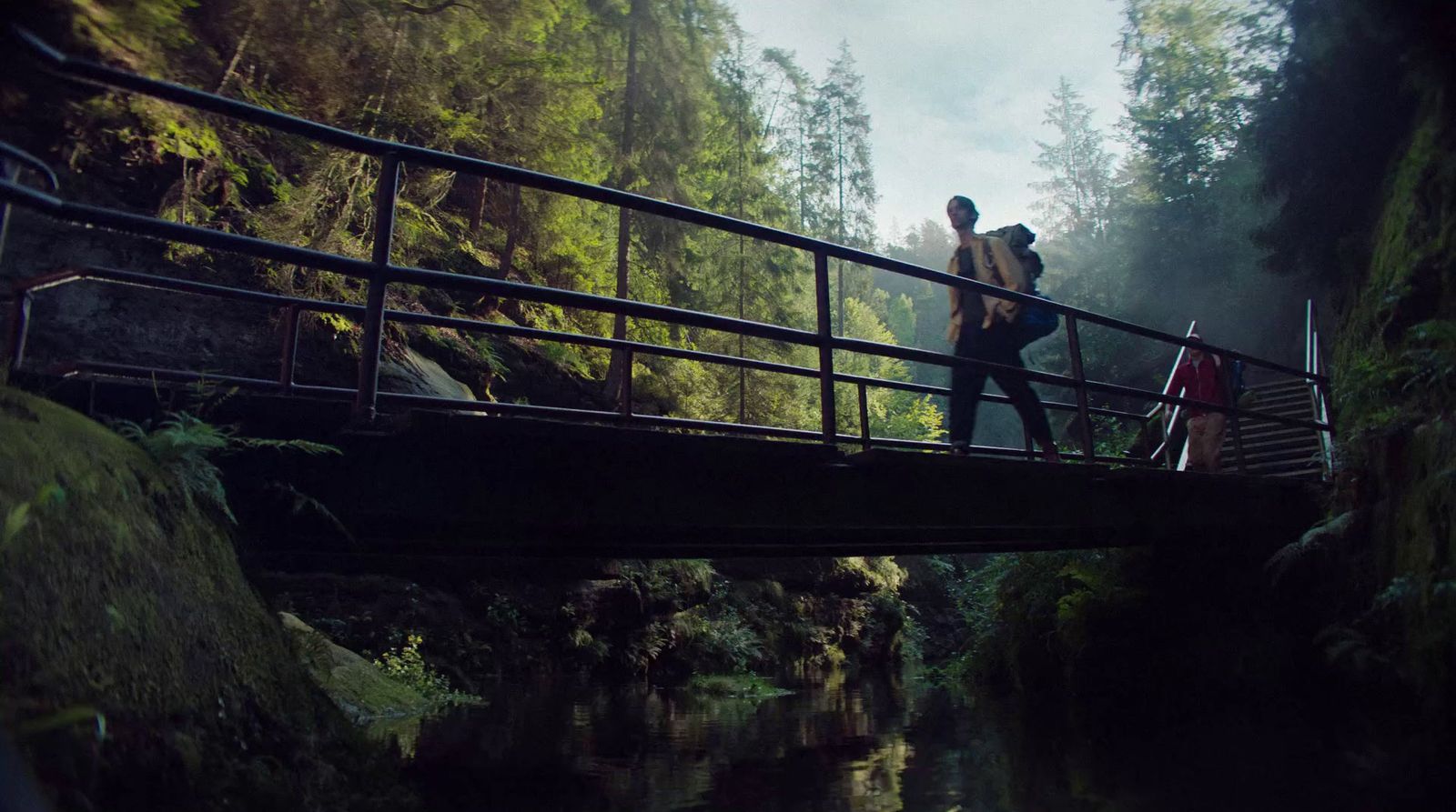 two people walking across a bridge over a river