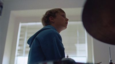 a young boy in a blue hoodie standing in front of a window