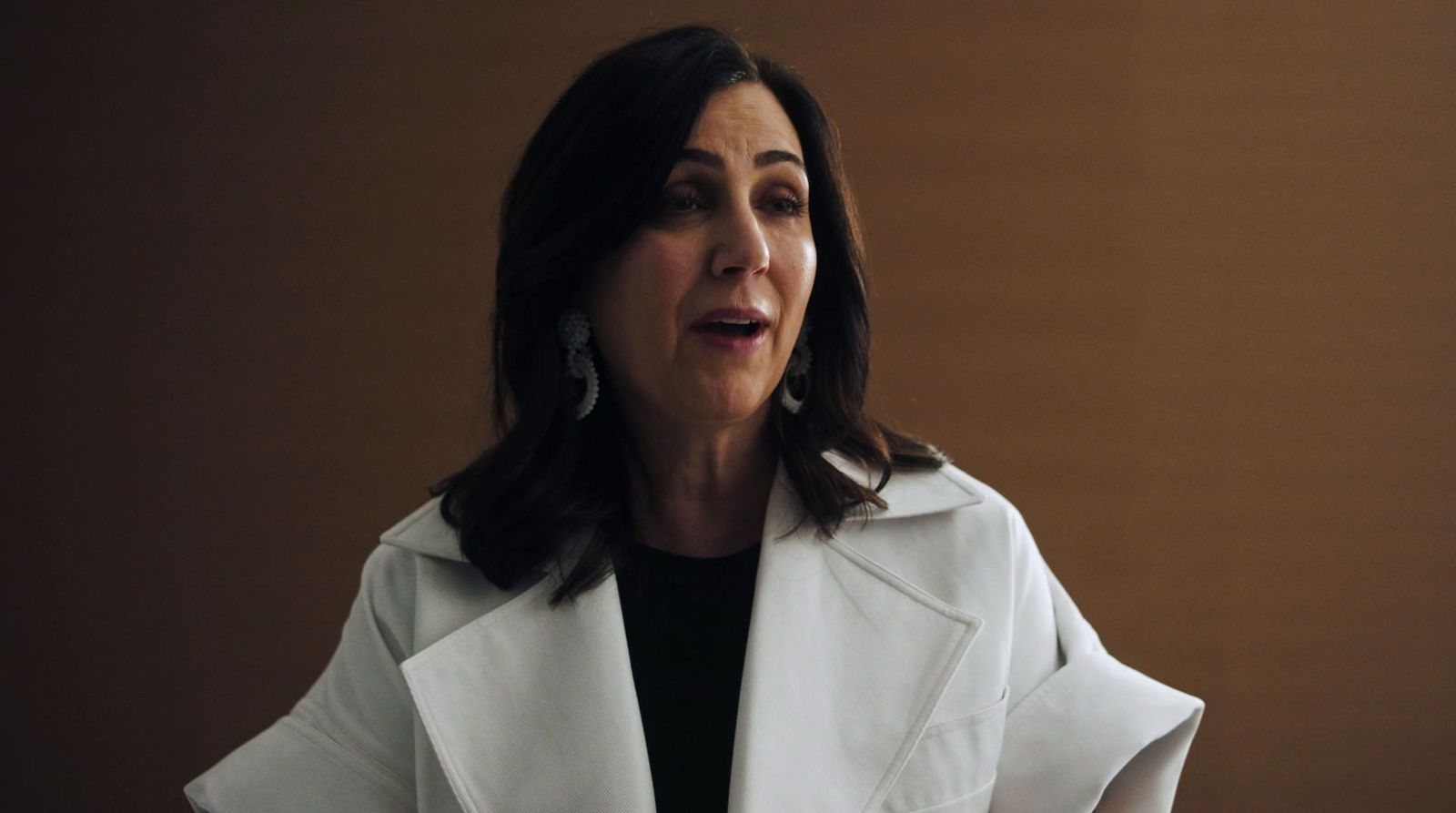 a woman wearing a white coat and earrings