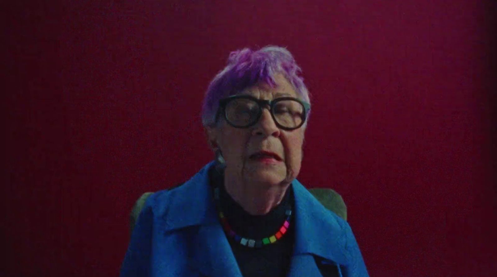 a woman with purple hair and glasses sitting in a chair