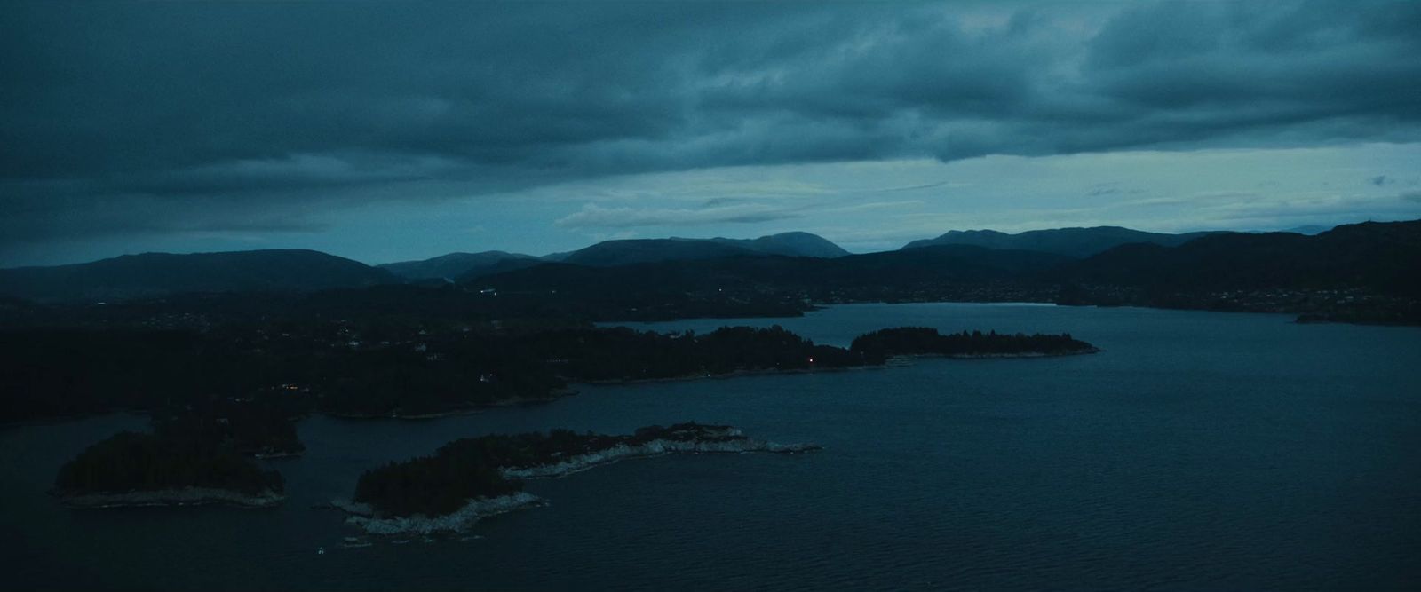 a body of water surrounded by mountains under a cloudy sky