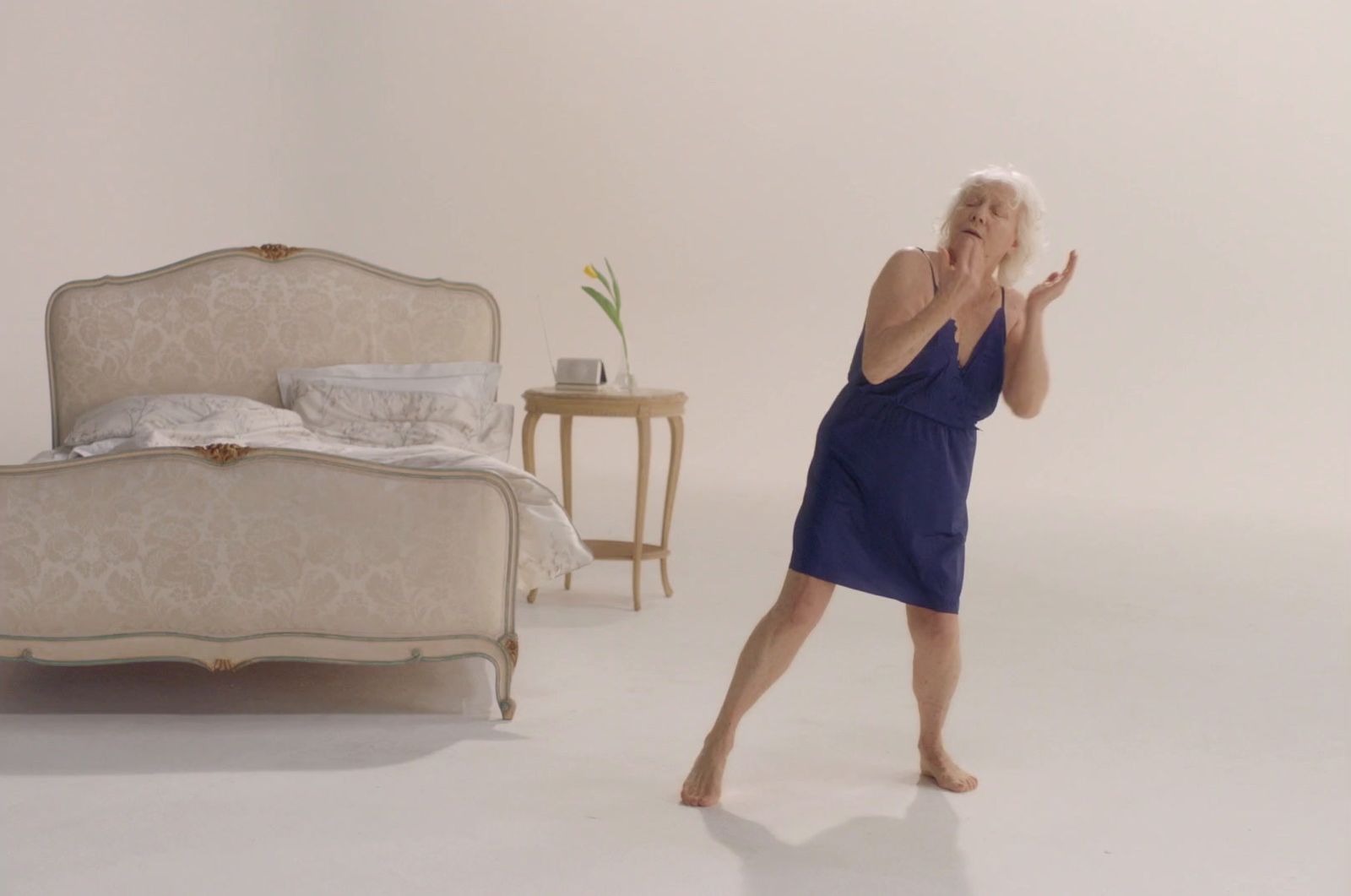 a woman in a blue dress standing in front of a bed