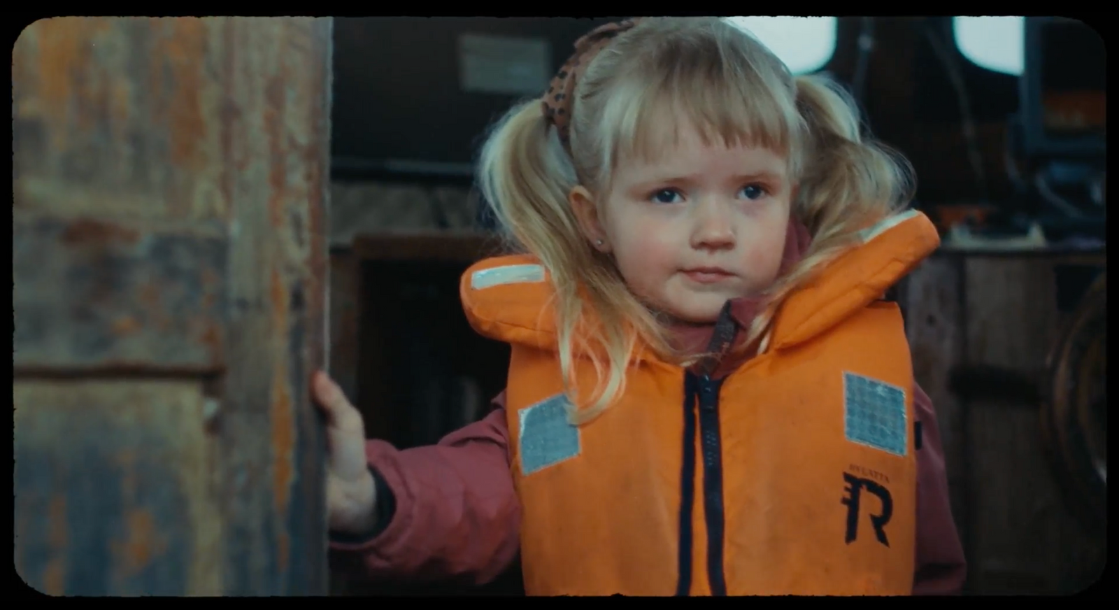 a little girl wearing an orange vest and pointing at the camera