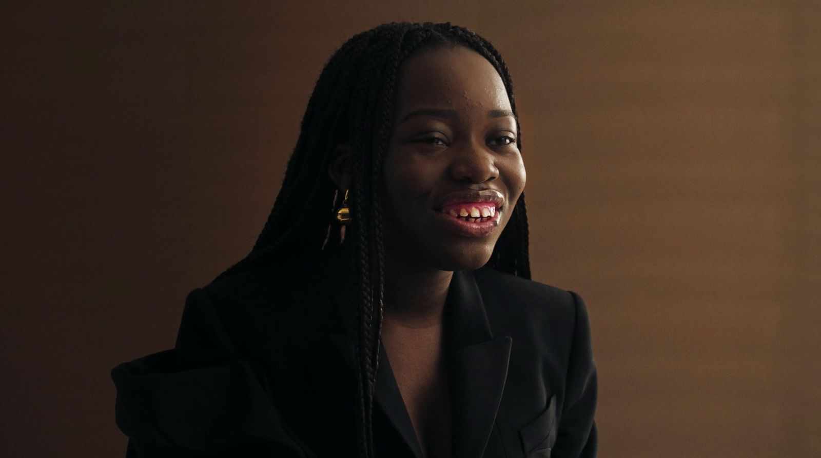 a woman with braids smiling and wearing a black jacket