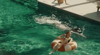 a woman riding a raft in a pool next to a dog