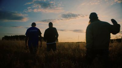 three men standing in a field watching the sun set