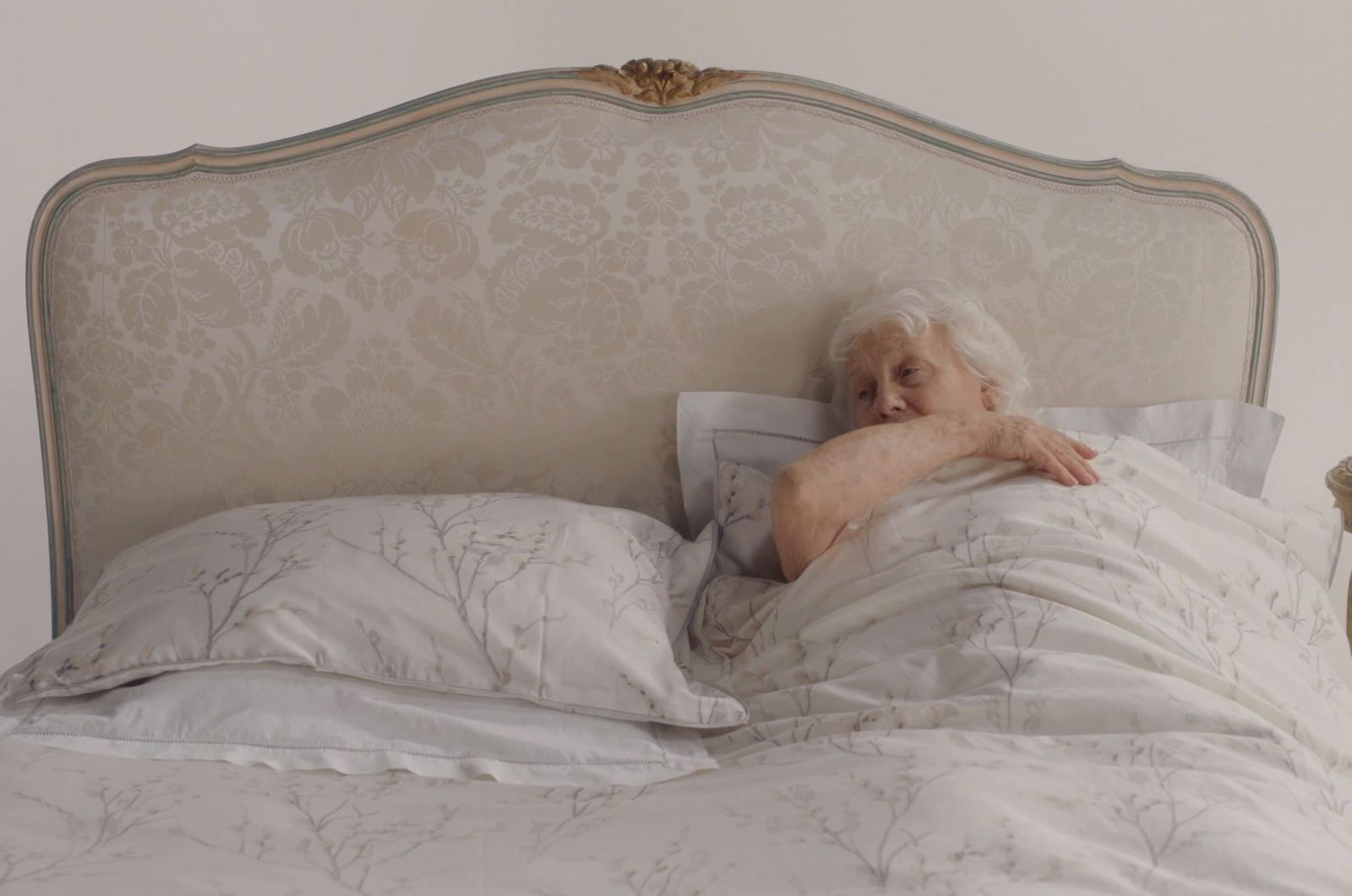 an old woman laying in bed with a white comforter