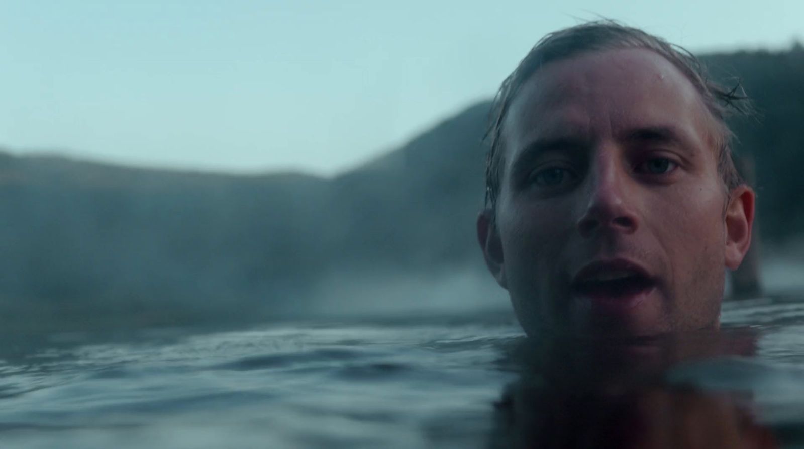 a man swimming in a lake with mountains in the background