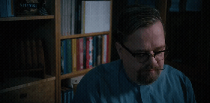 a man with glasses and a beard sitting in front of a book shelf