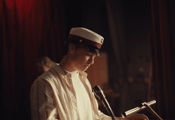 a man in a sailor's hat sitting in front of a microphone