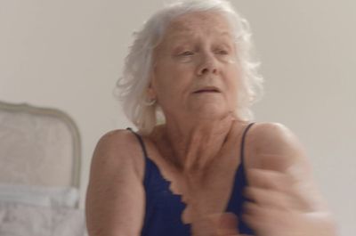 an older woman in a blue tank top brushing her teeth