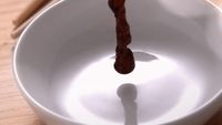 a wooden spoon pouring liquid into a white bowl