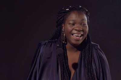 a woman with braids smiles while holding a microphone