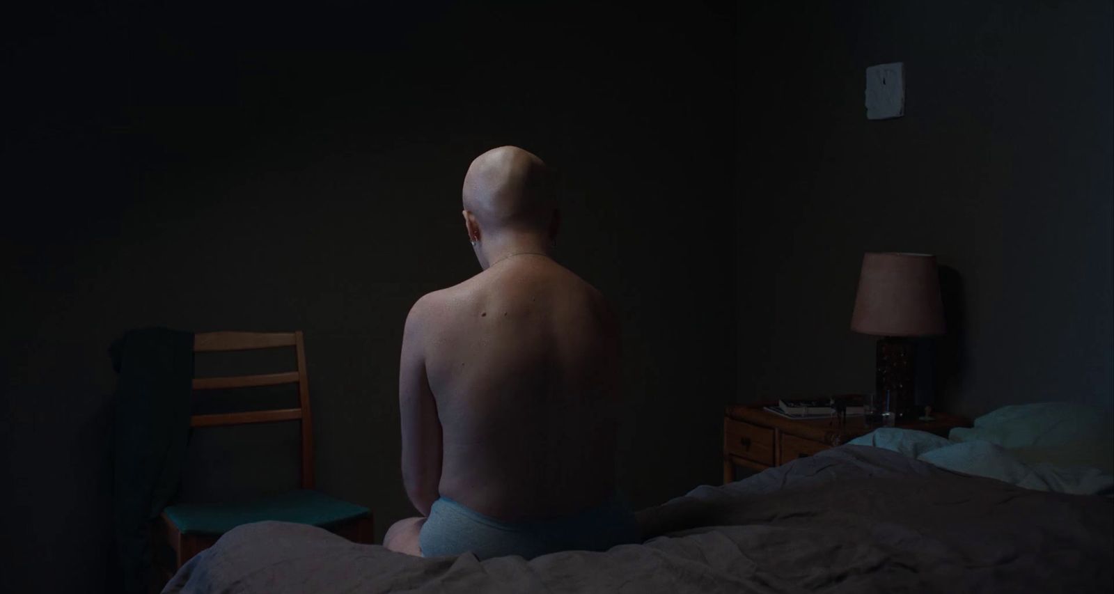 a naked man sitting on a bed in a dark room