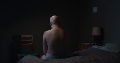 a naked man sitting on a bed in a dark room